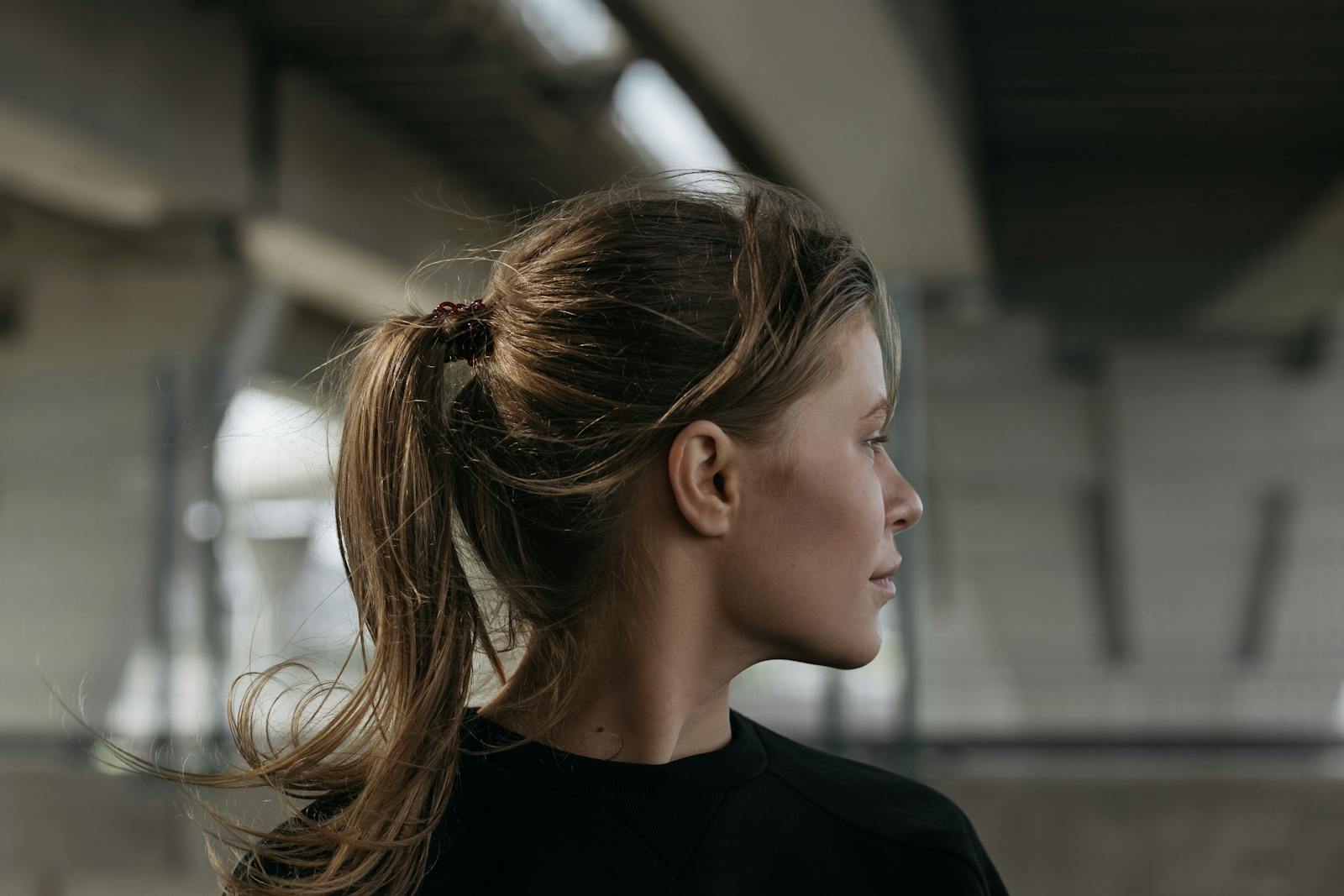Profile view of a woman with ponytail wearing a black shirt in an indoor setting.