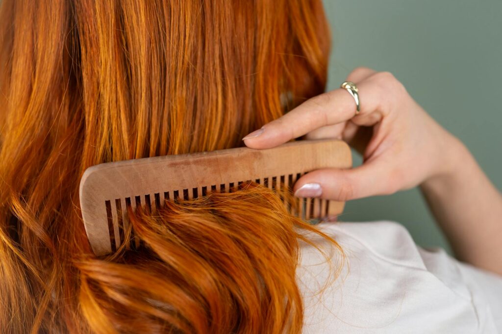 Close-up of a woman combing her long red hair with a wooden comb.